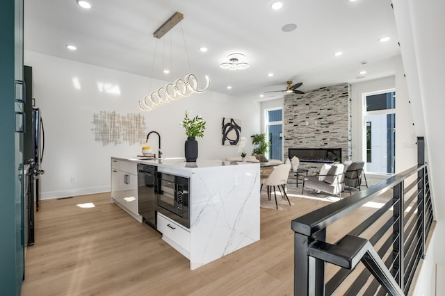 kitchen with sink, hanging light fixtures, a center island with sink, a fireplace, and black appliances