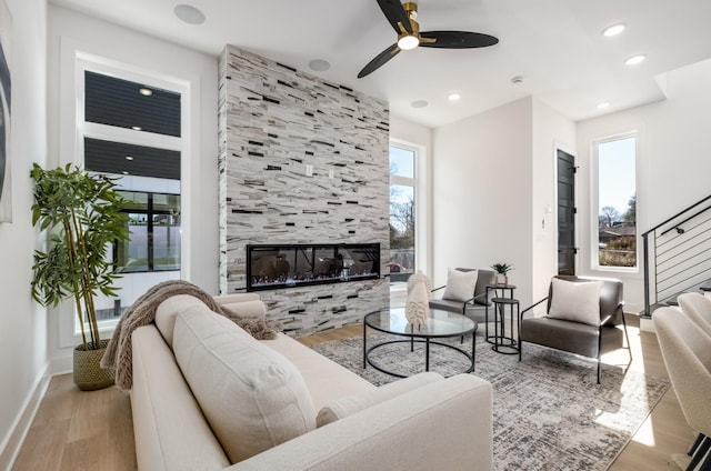 living room with a tiled fireplace, light hardwood / wood-style floors, and ceiling fan