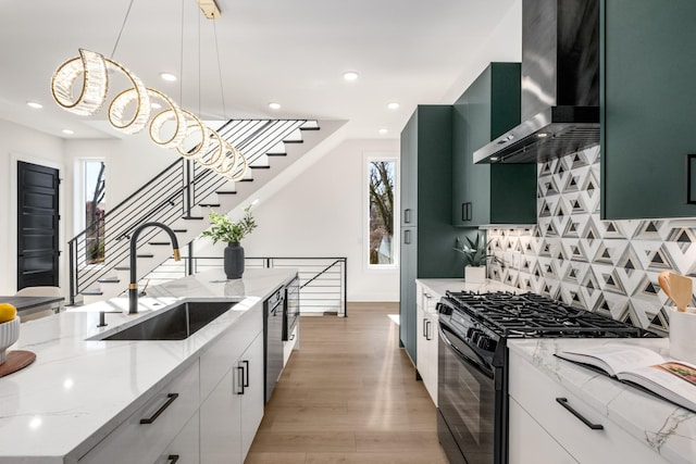 kitchen featuring black gas range oven, white cabinetry, sink, hanging light fixtures, and wall chimney exhaust hood