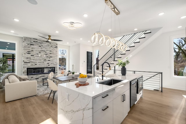 kitchen with sink, decorative light fixtures, an island with sink, a tiled fireplace, and white cabinets