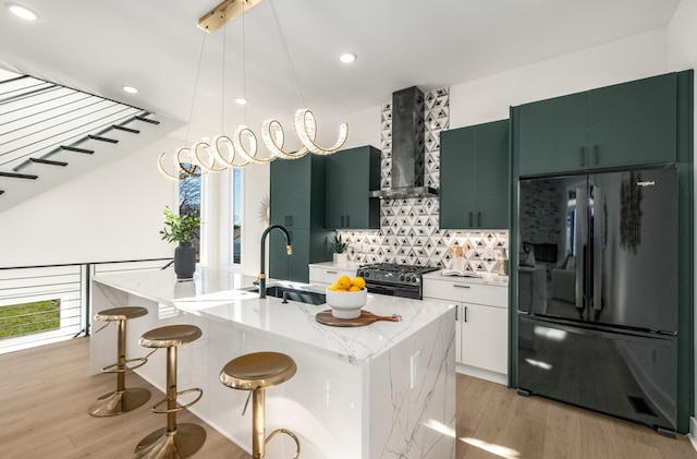 kitchen with black refrigerator, pendant lighting, range with gas stovetop, an island with sink, and light stone counters