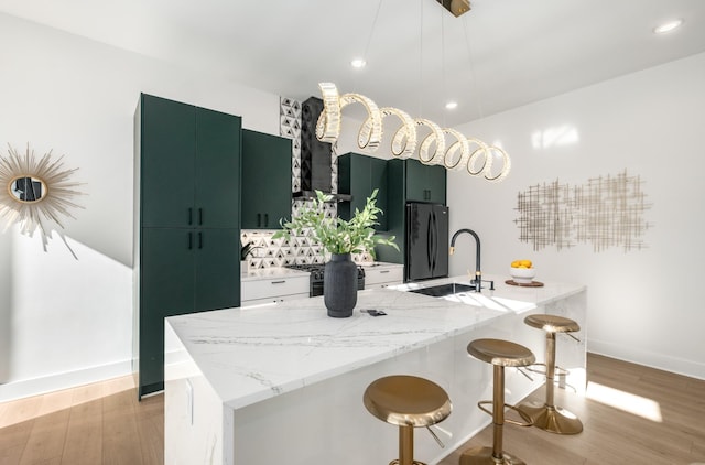 kitchen featuring light stone counters, decorative light fixtures, an island with sink, and black appliances