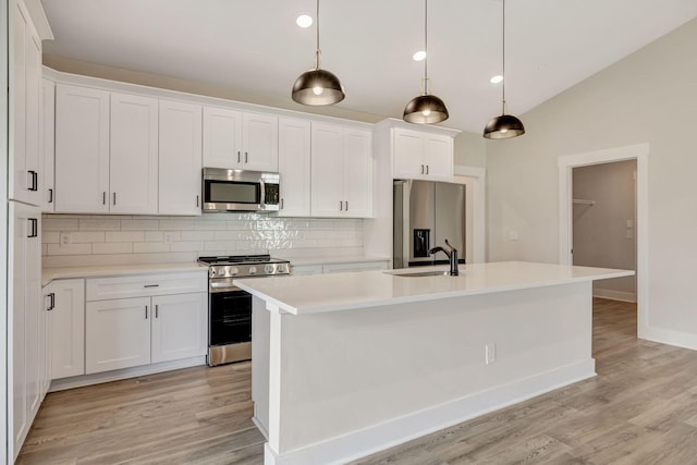 kitchen featuring appliances with stainless steel finishes, white cabinetry, sink, hanging light fixtures, and a center island with sink