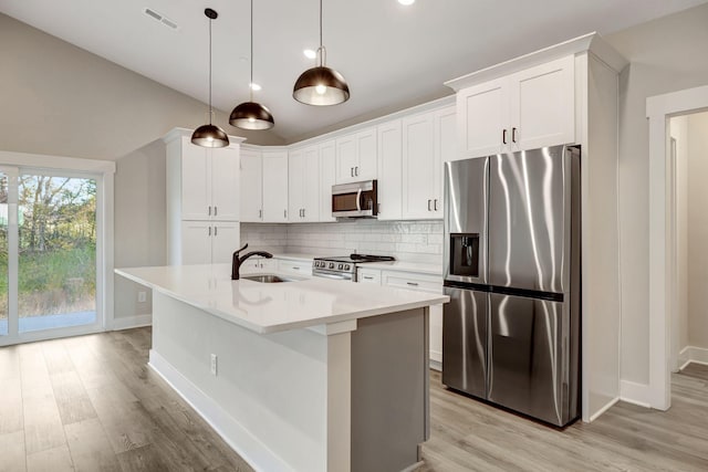 kitchen with appliances with stainless steel finishes, decorative light fixtures, sink, white cabinets, and a center island with sink