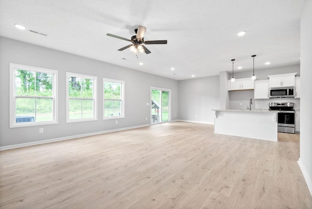 unfurnished living room with ceiling fan, sink, and light wood-type flooring