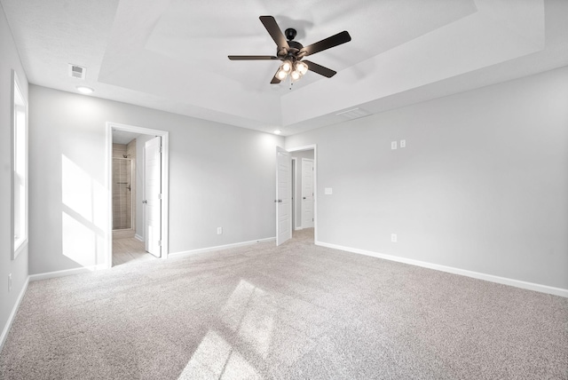 unfurnished bedroom featuring a raised ceiling, light colored carpet, and ensuite bath