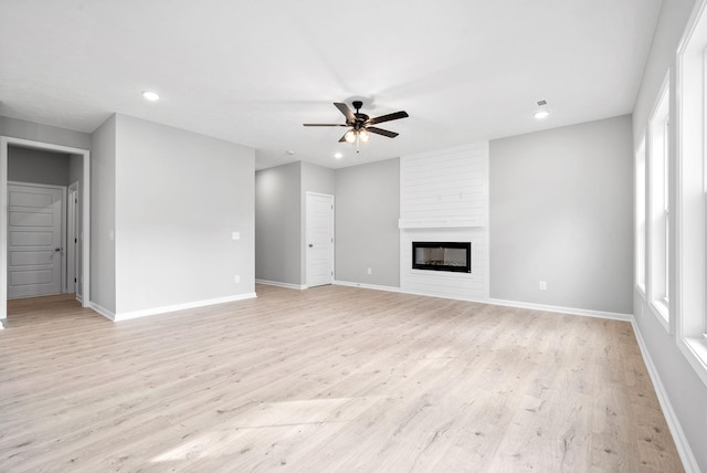 unfurnished living room with ceiling fan, a large fireplace, and light hardwood / wood-style floors