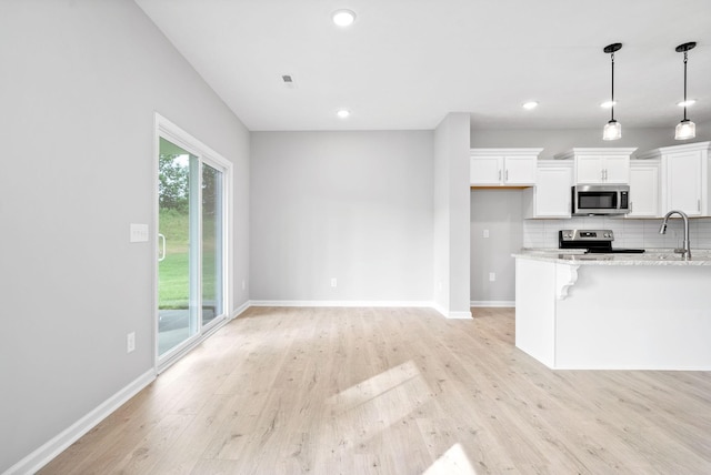 kitchen featuring pendant lighting, appliances with stainless steel finishes, light stone countertops, and white cabinets