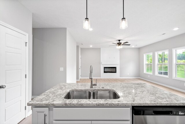 kitchen with sink, hanging light fixtures, dishwasher, a fireplace, and light stone countertops