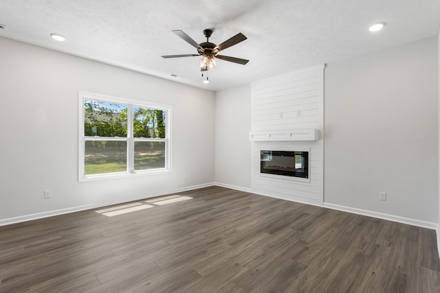 unfurnished living room featuring dark hardwood / wood-style flooring, ceiling fan, a large fireplace, and a textured ceiling