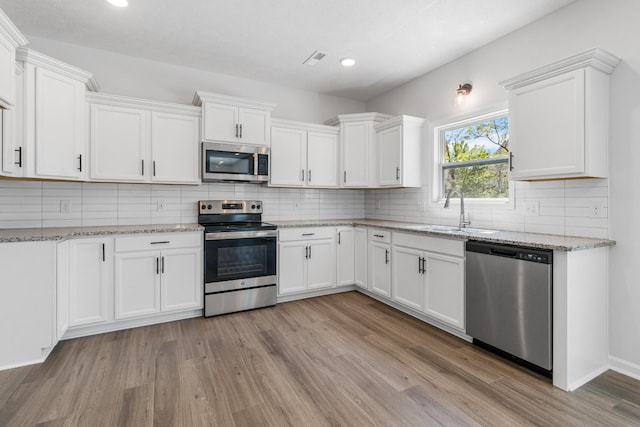 kitchen with appliances with stainless steel finishes, sink, white cabinets, light stone counters, and light hardwood / wood-style flooring