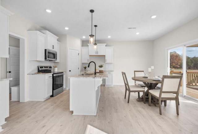 kitchen with sink, light stone counters, decorative light fixtures, stainless steel appliances, and a kitchen island with sink