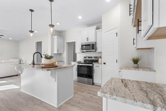 kitchen with pendant lighting, appliances with stainless steel finishes, light hardwood / wood-style floors, white cabinets, and a center island with sink