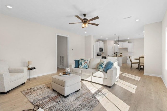 living room featuring sink, ceiling fan, and light wood-type flooring