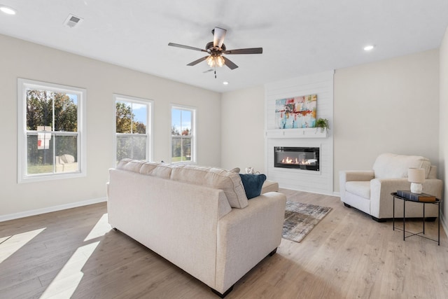 living room featuring ceiling fan, a fireplace, and light hardwood / wood-style flooring