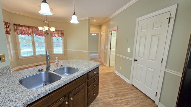 kitchen with sink, dark brown cabinetry, light stone counters, light hardwood / wood-style floors, and decorative light fixtures