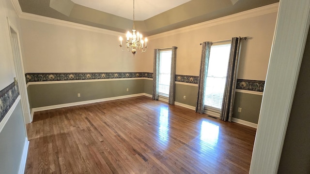 empty room with dark wood-type flooring, ornamental molding, a tray ceiling, and a chandelier