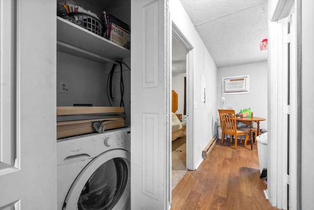 clothes washing area with washer / clothes dryer, a baseboard radiator, a wall mounted AC, light hardwood / wood-style floors, and a textured ceiling