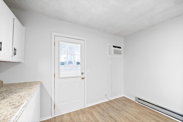 interior space with a baseboard radiator, a wall mounted AC, a textured ceiling, and light wood-type flooring