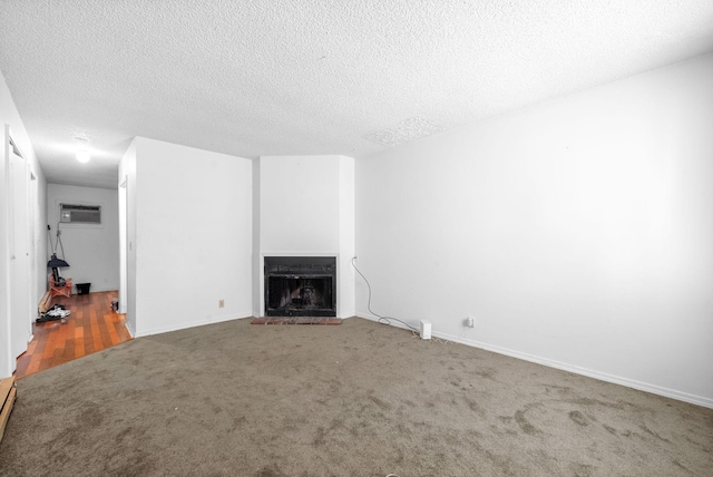 unfurnished living room with a brick fireplace, a wall mounted AC, carpet, and a textured ceiling