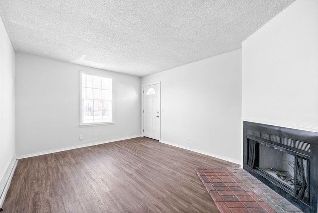 unfurnished living room with a baseboard heating unit, dark wood-type flooring, a textured ceiling, and a fireplace