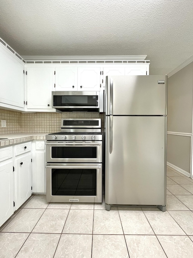 kitchen with a textured ceiling, light tile patterned floors, white cabinets, stainless steel appliances, and backsplash