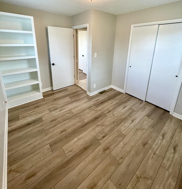 unfurnished bedroom featuring a textured ceiling, a closet, and light wood-type flooring