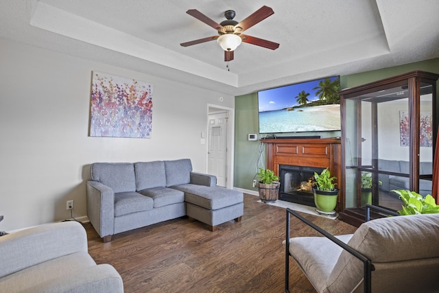 living room featuring dark wood-type flooring, ceiling fan, a raised ceiling, and a textured ceiling