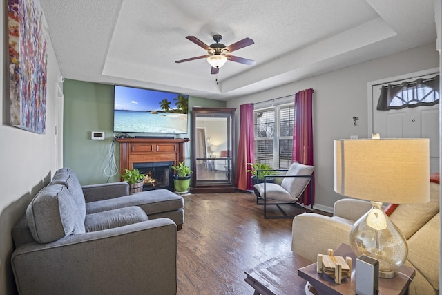 living room with a raised ceiling, ceiling fan, a textured ceiling, and dark hardwood / wood-style flooring