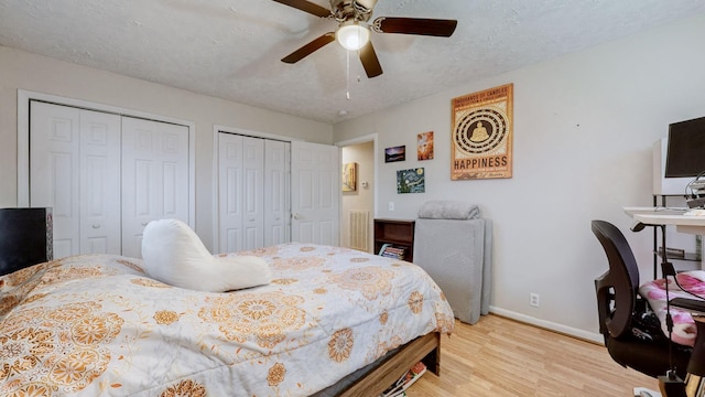 bedroom with ceiling fan, light hardwood / wood-style floors, a textured ceiling, and two closets