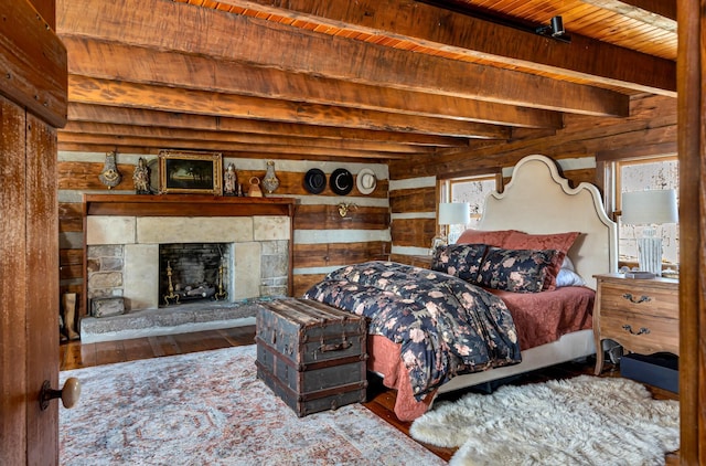 bedroom with a stone fireplace, wooden walls, beamed ceiling, wood-type flooring, and wooden ceiling