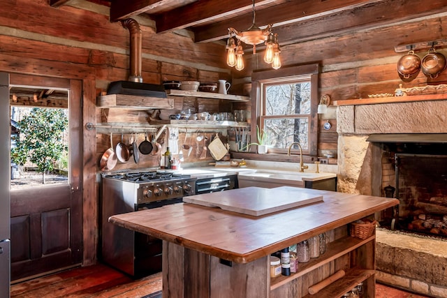 kitchen with sink, wooden walls, a fireplace, stainless steel range with gas cooktop, and custom exhaust hood