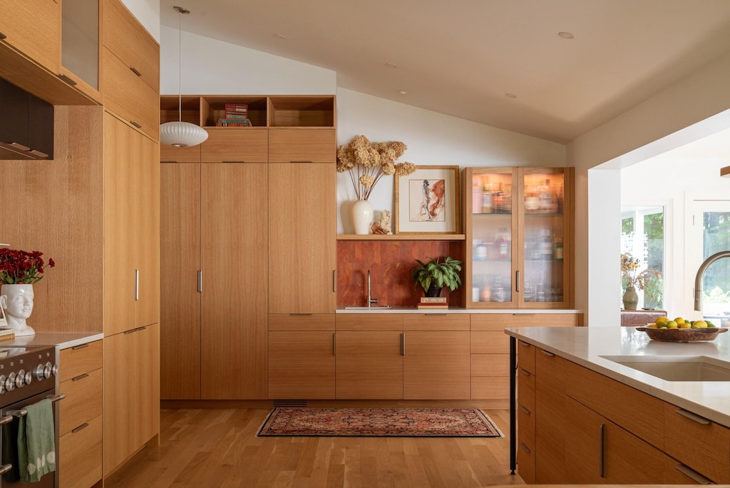 kitchen with pendant lighting, lofted ceiling, sink, range, and light wood-type flooring