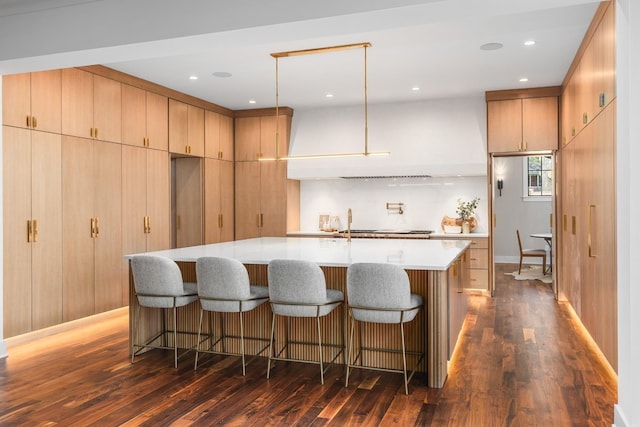 kitchen featuring hanging light fixtures, a kitchen island with sink, light brown cabinetry, and dark hardwood / wood-style flooring