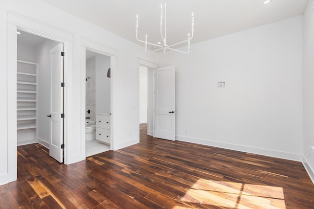 unfurnished bedroom featuring dark wood-type flooring, an inviting chandelier, ensuite bath, a spacious closet, and a closet