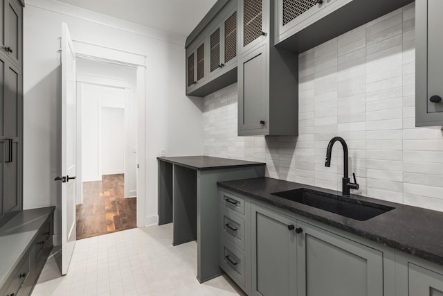 kitchen with sink, crown molding, gray cabinets, backsplash, and dark stone counters