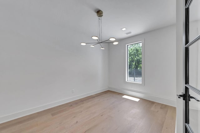 spare room featuring an inviting chandelier and light hardwood / wood-style floors