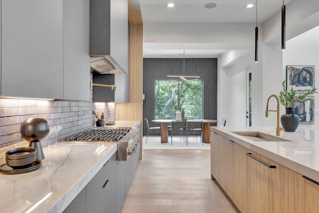 kitchen featuring stainless steel gas cooktop, sink, hanging light fixtures, light stone countertops, and backsplash