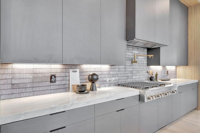 kitchen featuring light stone counters, light hardwood / wood-style flooring, gray cabinets, stainless steel gas stovetop, and backsplash