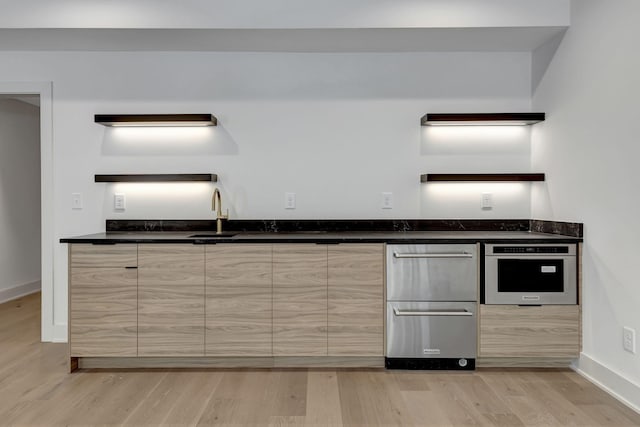 kitchen with light brown cabinetry, oven, sink, and light hardwood / wood-style flooring