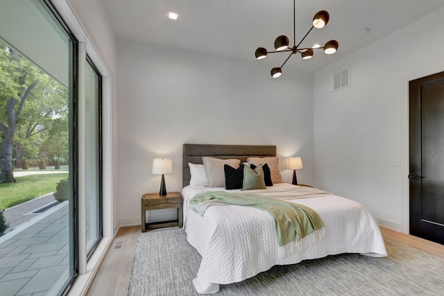 bedroom featuring an inviting chandelier, access to exterior, and light hardwood / wood-style floors