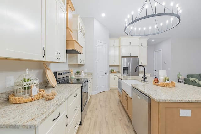 kitchen featuring white cabinetry, appliances with stainless steel finishes, light stone countertops, and a large island with sink