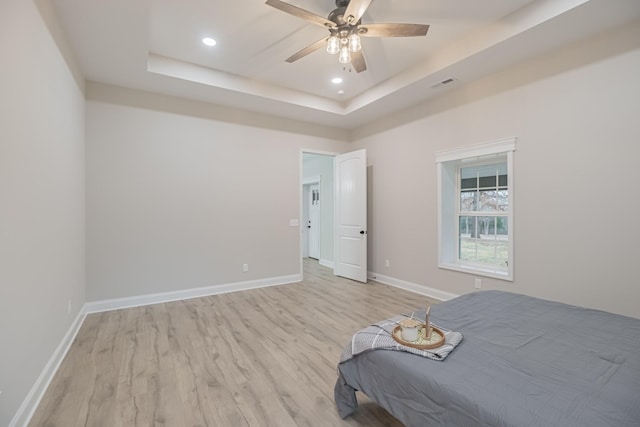 unfurnished bedroom with a raised ceiling, ceiling fan, and light hardwood / wood-style floors