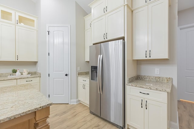 kitchen with stainless steel refrigerator with ice dispenser, white cabinets, light stone counters, and light hardwood / wood-style flooring