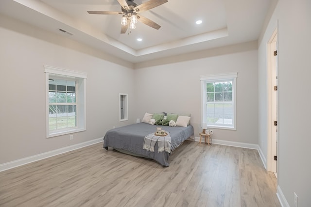 bedroom featuring ceiling fan, a tray ceiling, and light wood-type flooring