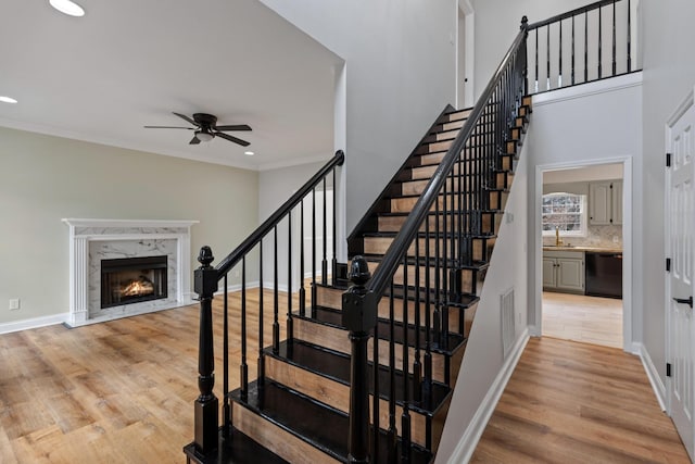 stairs with sink, crown molding, hardwood / wood-style flooring, ceiling fan, and a high end fireplace