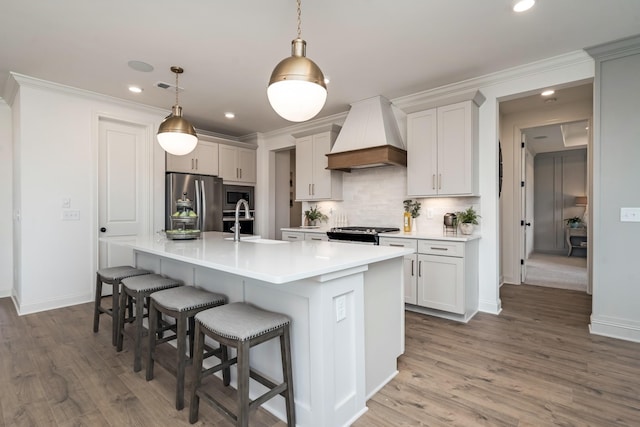 kitchen featuring premium range hood, a center island with sink, a kitchen breakfast bar, pendant lighting, and stainless steel appliances