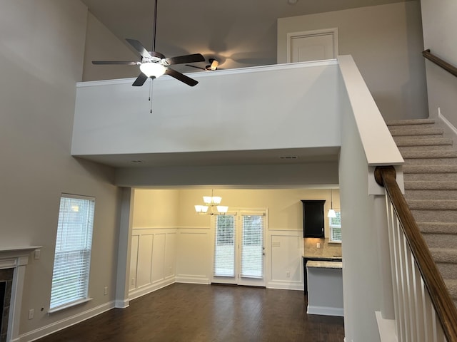 unfurnished living room with dark wood-type flooring, a tile fireplace, a wealth of natural light, ceiling fan with notable chandelier, and a high ceiling