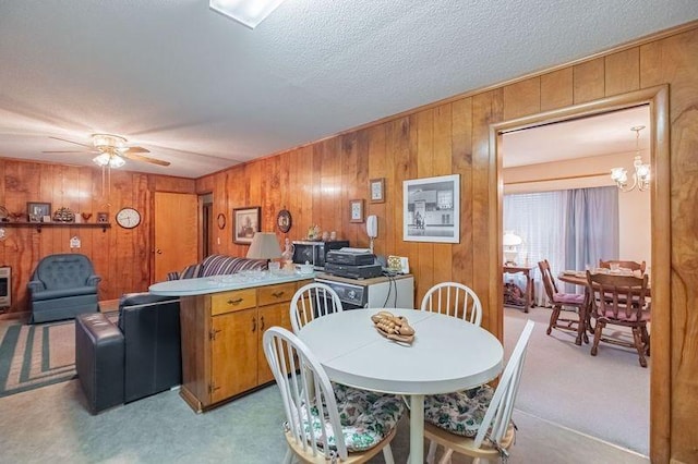 dining area with light carpet, ceiling fan with notable chandelier, a textured ceiling, and wood walls