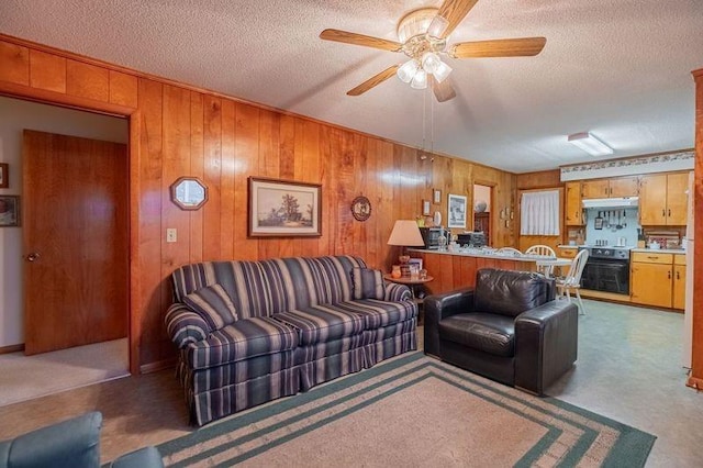 carpeted living room with ceiling fan, a textured ceiling, and wood walls